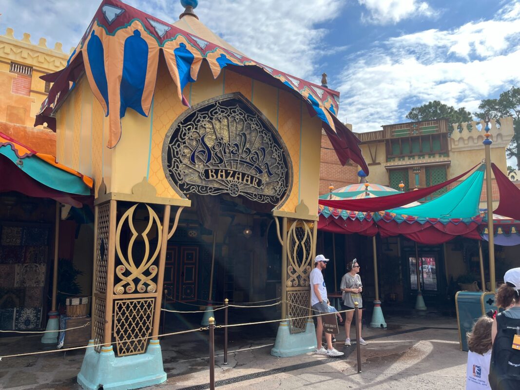 Visitors stand outside a bazaar with colorful awnings and ornate decorations on a sunny day.