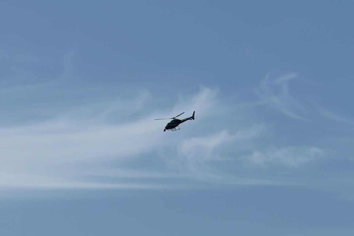 A helicopter flying in the sky with light clouds in the background.