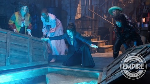 A group of four people in theatrical costumes surrounds a glowing blue pit inside a dimly-lit room. The "Empire Exclusive" logo graces the bottom right corner. Fans will instantly recognize the vibe, echoing themes from "Agatha All Along.