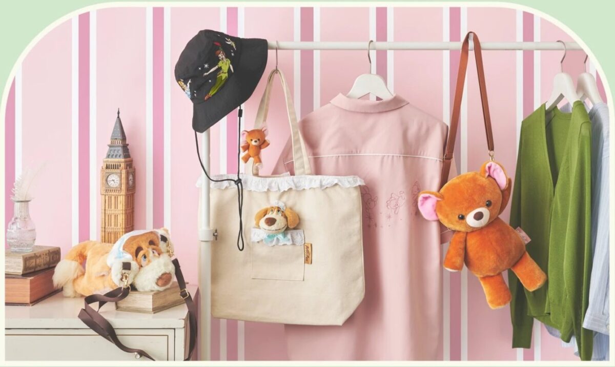 A clothing rack holds a pink dress, green sweater, bucket hat, tote bag with a plush toy, and Michael's Teddy Bear bag. Nearby, stuffed animals and a model of Big Ben decorate a shelf against a pink-striped wall.