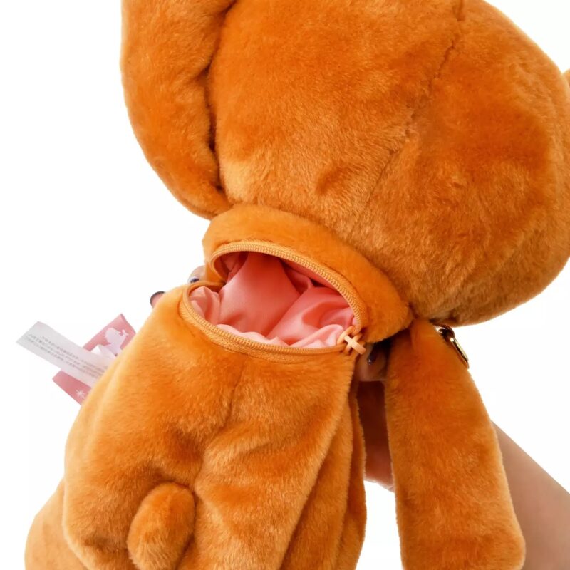 A close-up of an orange plush toy with a zippered compartment on its back, revealing a pink interior.