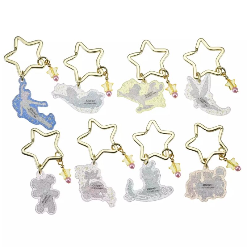 A set of eight star-shaped keychains, each featuring a glittery silhouette of different Disney characters, including Peter Pan, Tinkerbell, and others. Each keychain has a small golden star and a pink bead.