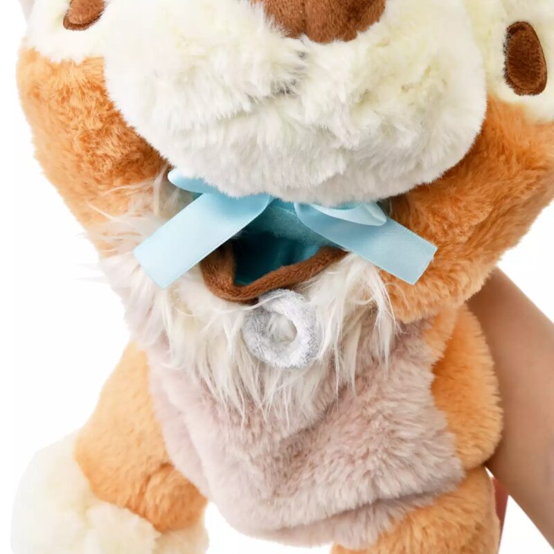 A close-up of a plush toy with brown and white fur, displaying a tied blue ribbon near its neck.