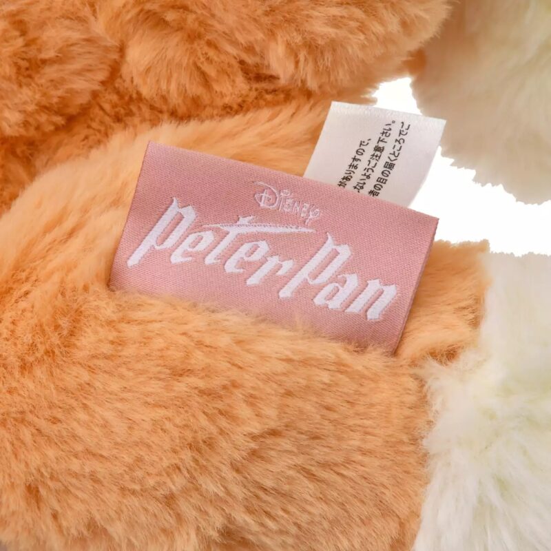 Close-up of a fluffy toy's label with the text "Disney Peter Pan" in white on a pink background, alongside a white care tag with text in another language.