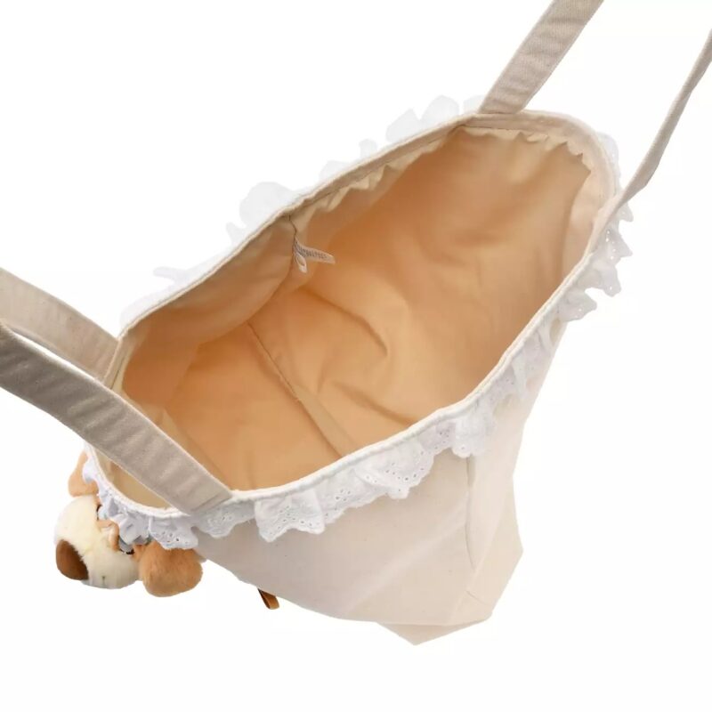 A beige shoulder bag with lace trim, showing its empty interior, and a small stuffed animal keychain attached to the handle.