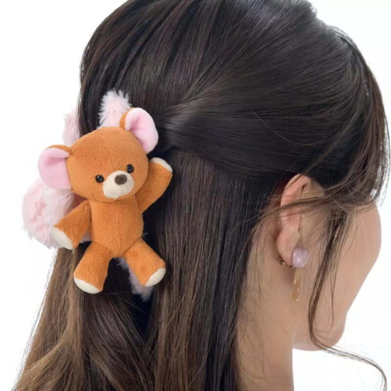 A woman with brown hair wears a plush teddy bear hair accessory clipped to the back of her head.