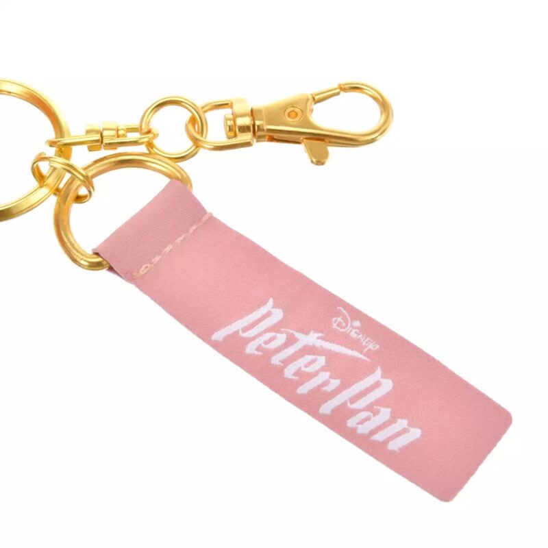 A keychain with gold hardware and a pink fabric tag that reads "Disney Peter Pan" in white text.