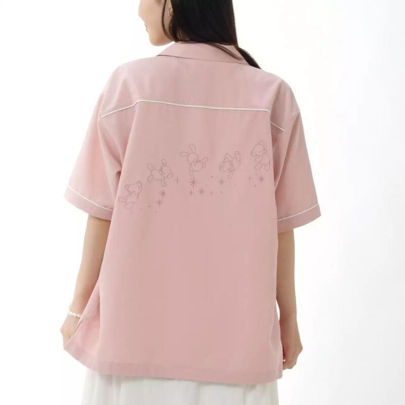 A woman wearing a pink button-up shirt with white trim and an embroidered design of mice and stars on the back.