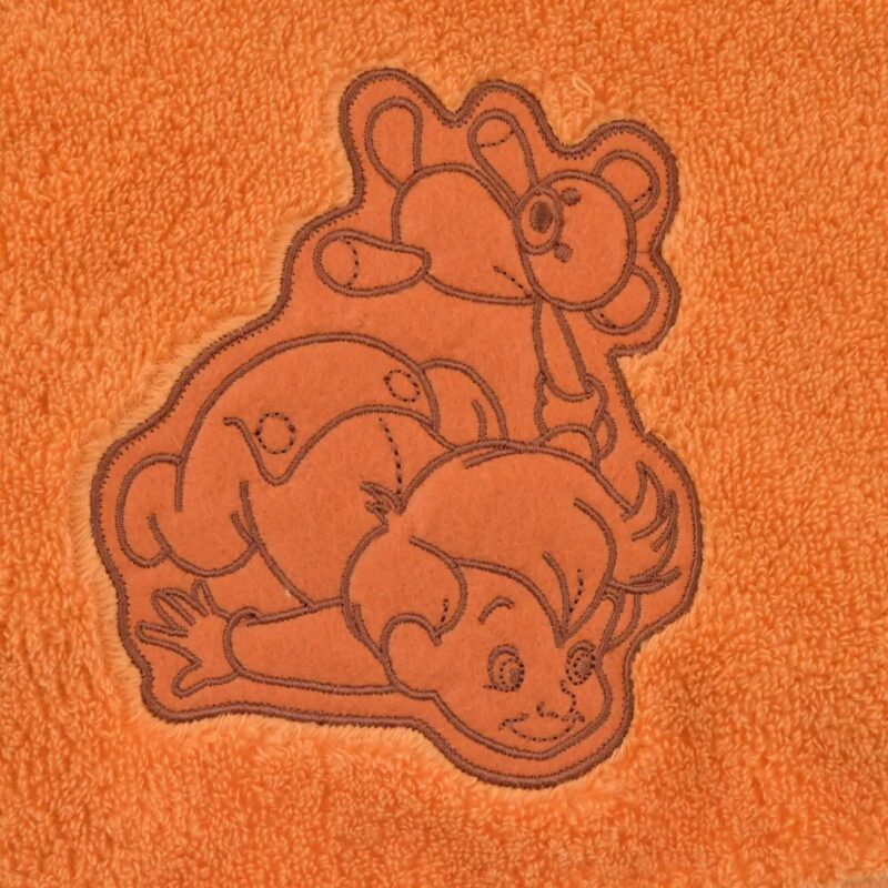 An orange towel features a stitched outline of a cartoon child playing with two teddy bears.