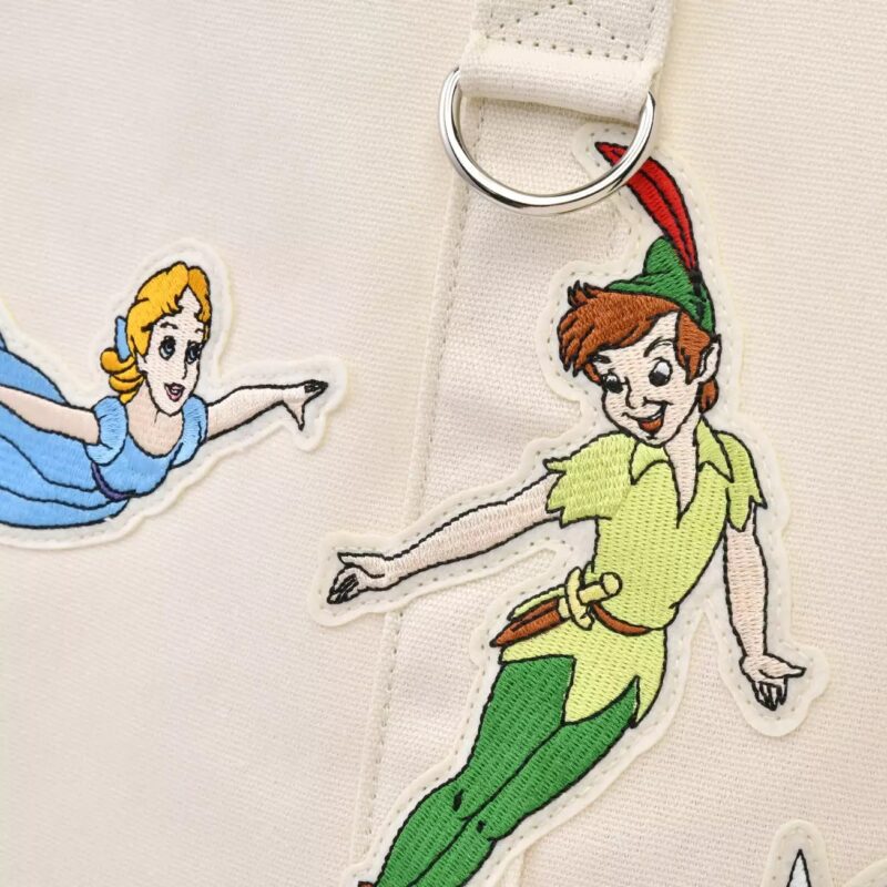 Embroidered designs of two animated characters, a boy in a green outfit with a red feather hat and a girl in a blue dress, on a light-colored fabric background with a metal ring detail.