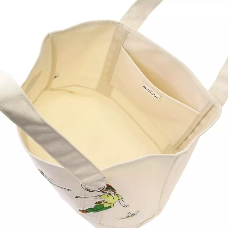 Image of an open, cream-colored tote bag with an interior pocket and playful illustrations of a person and a bird on the inner fabric. The bag has wide straps for carrying.