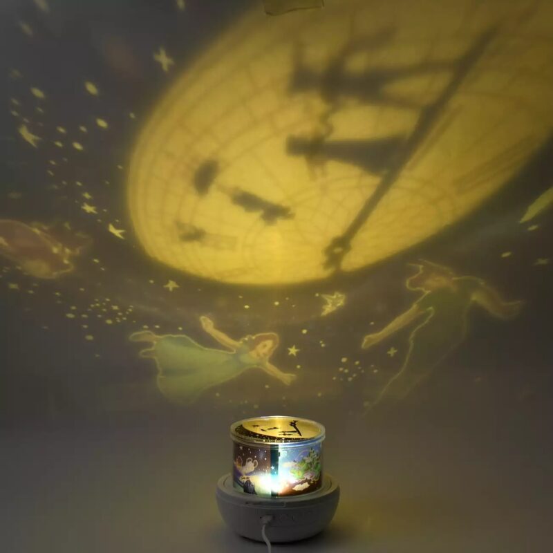 A night light projector casts whimsical silhouettes of Peter Pan, Wendy, and other magical elements onto a dimly lit wall.