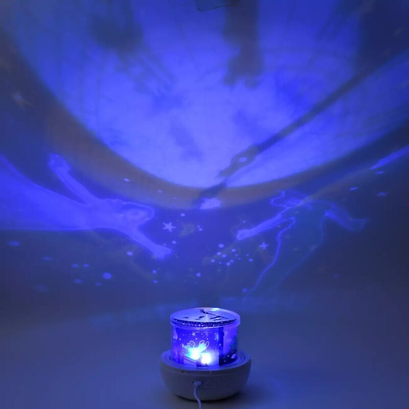 A blue star projector lamp casts glowing patterns of stars and celestial figures on the wall and ceiling in a dimly lit room.