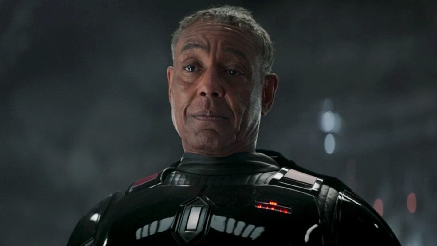 Giancarlo Esposito as Moff Gideon, a black man with short gray hair wearing a black futuristic suit with red and white lights on the chest in a dark environment.