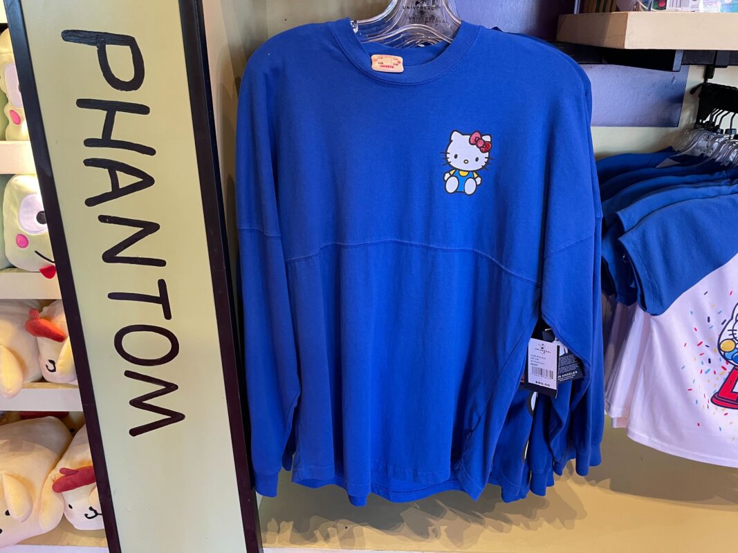 A blue Spirit Jersey with a small Hello Kitty graphic on the left chest is displayed on a clothing rack. The word "PHANTOM" is written vertically on a sign next to the sweatshirt, making it a unique find at Universal Orlando Resort.