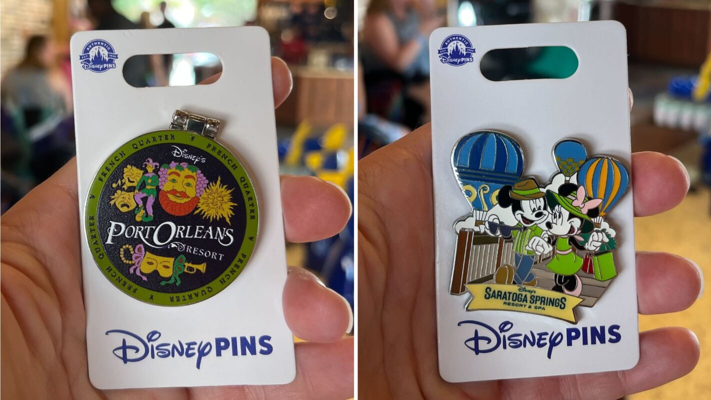 Close-up of two Disney pins being held, one depicting Port Orleans Resort with masks and the other showing Mickey and Minnie Mouse at Saratoga Springs with hot air balloons in the background.