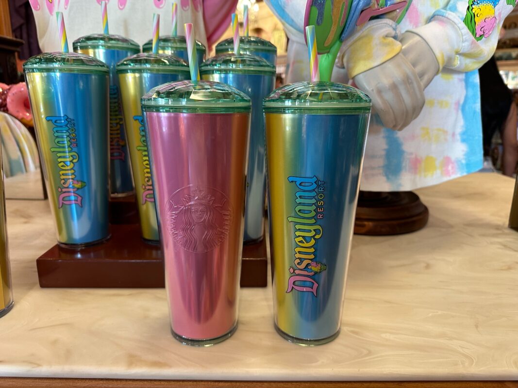 A collection of colorful tumblers, some with a Starbucks logo and others with a Disneyland Resort logo, displayed on a wooden table.