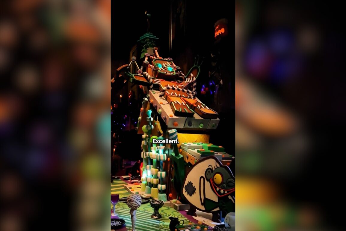 A brightly colored, whimsical gingerbread house with detailed decorations and a dragon head on top. Text in the center reads "Excellent." Various blurred objects are visible in the foreground.