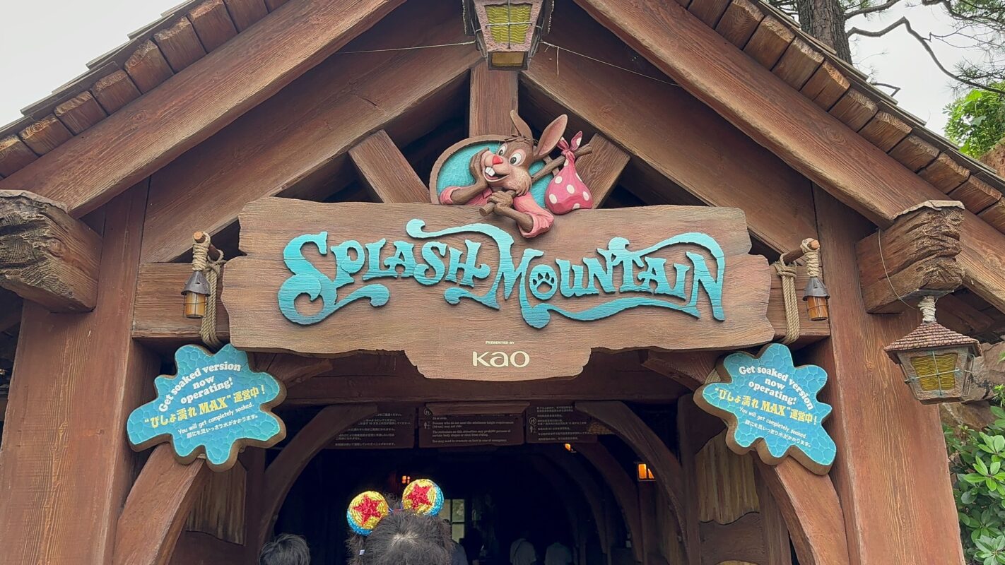 Entrance to Splash Mountain featuring a wooden sign with a character above it and blue cloud-shaped notices on either side.