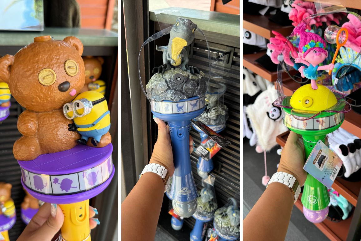 A hand holds three character-themed reactive bubble wands in a store. The wands feature a teddy bear and minion, a character on a rock with a spaceship, and a colorful character on a yellow spinning top.
