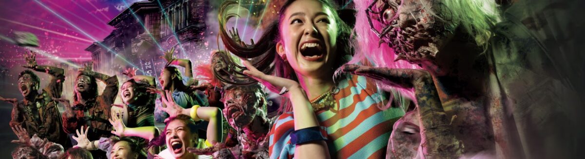 A woman screams and smiles, surrounded by zombies and a vibrant, haunted house-themed background, with flashes of pink and green lights. Other people in the background also display expressions of surprise and thrill.