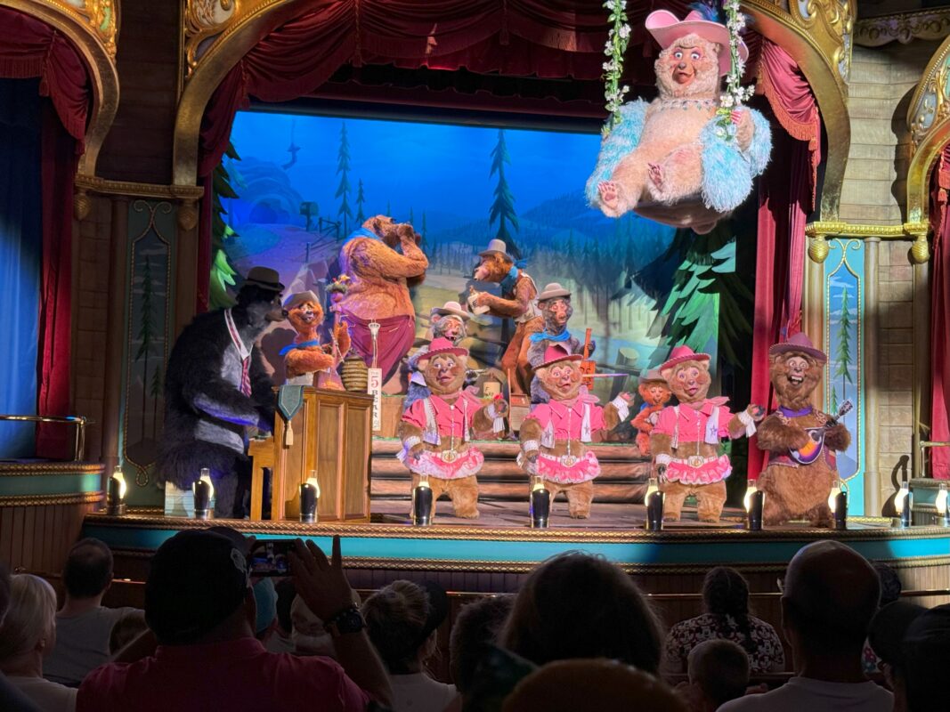 Animatronic bear characters perform a lively country bear musical jamboree on a theater stage, with various bear figures playing instruments and singing under bright stage lights.