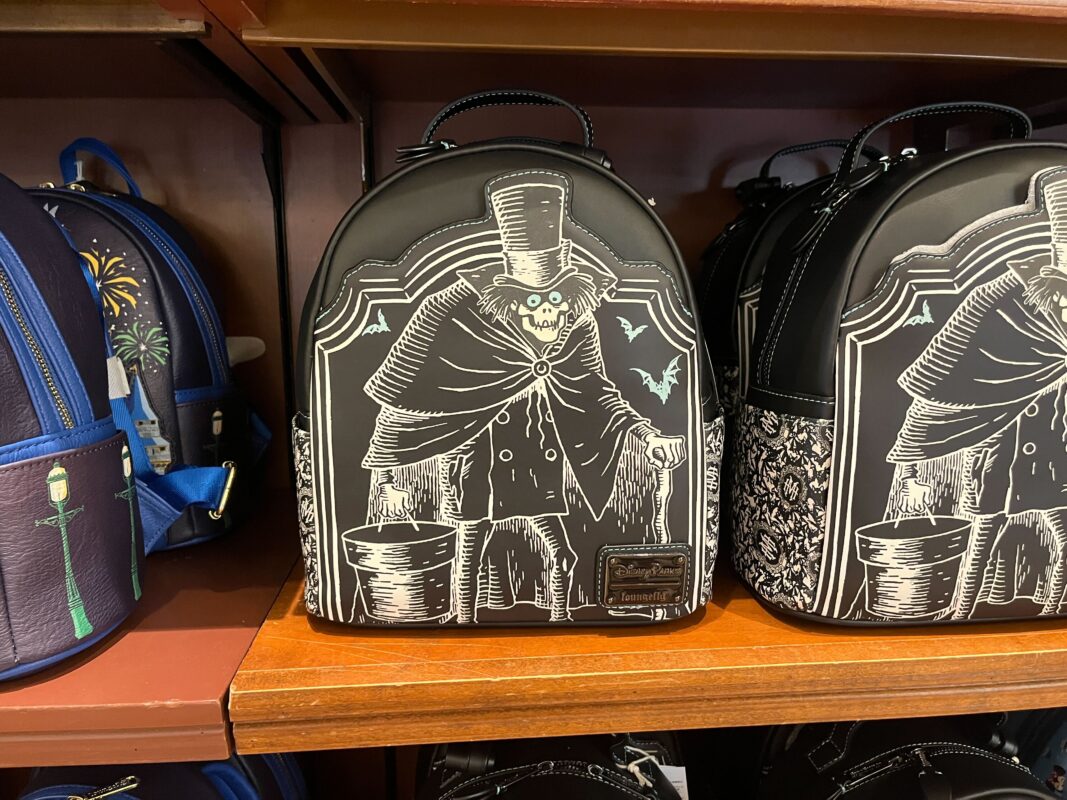 A black backpack featuring a sinister ghostly figure in a top hat with glowing eyes and a bat on the side is displayed on a store shelf. Other themed backpacks are seen nearby.