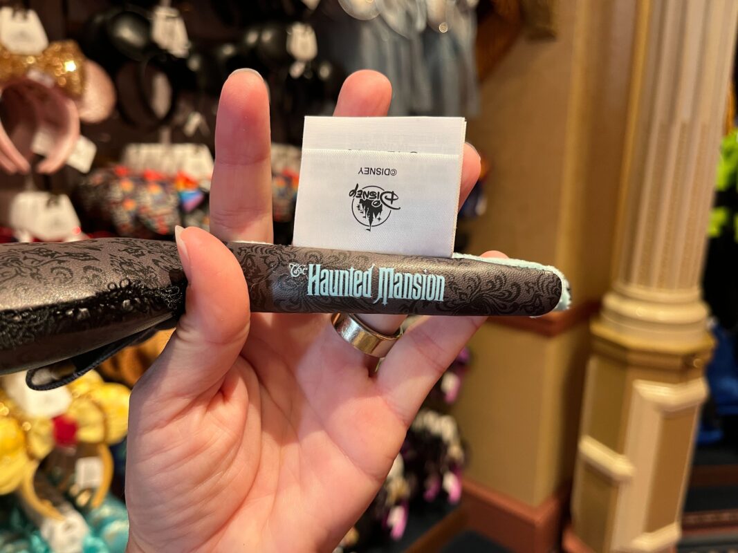 A person holds up a black pen with "The Haunted Mansion" text in a store. Other merchandise is visible in the background.