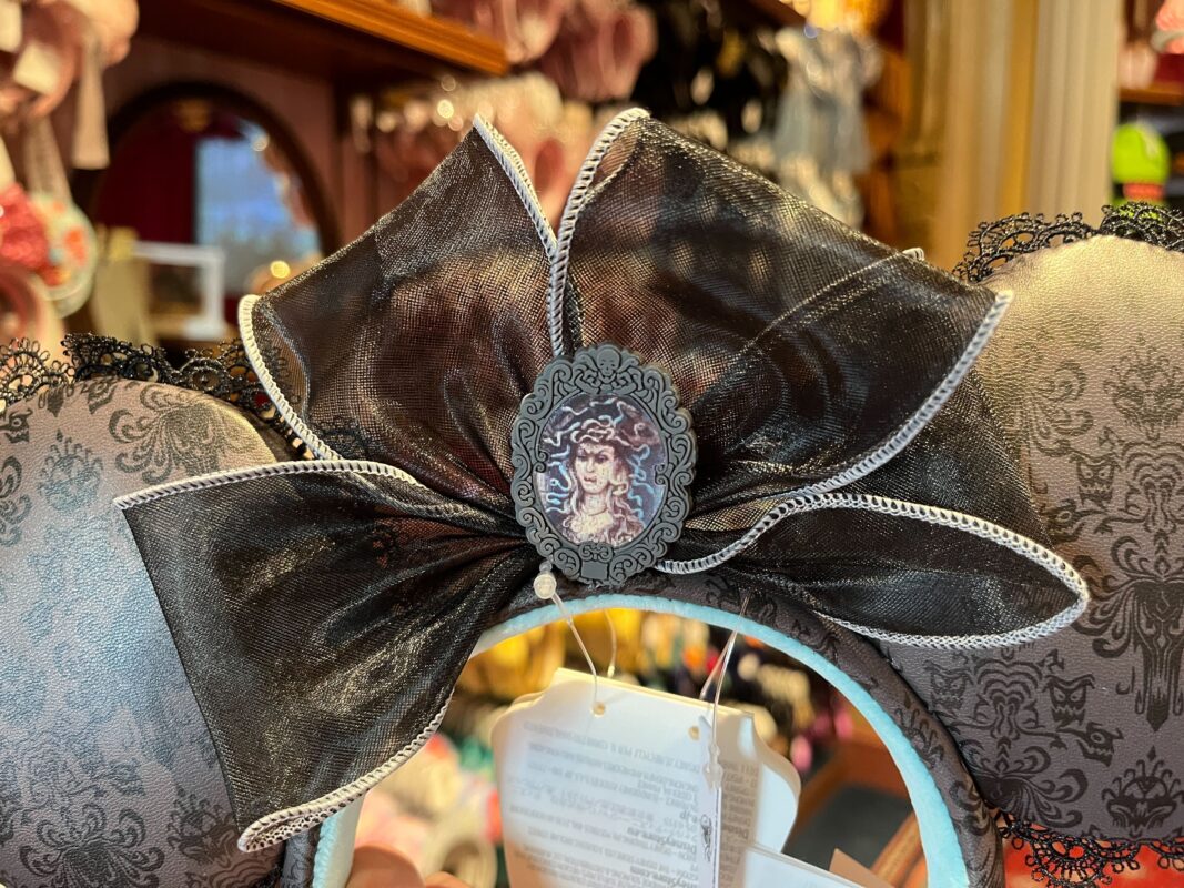 A decorative headband with lace, organza bow, and a vintage-style cameo brooch displayed in a store.