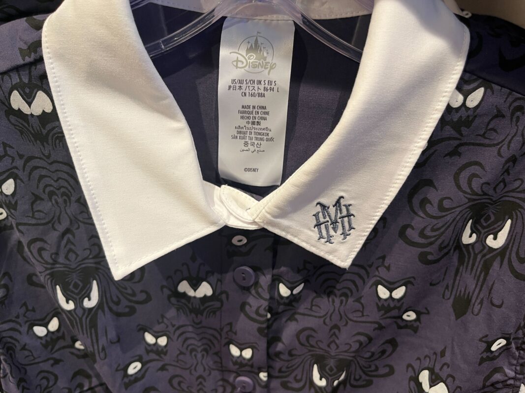 Close-up of a shirt with a white collar and patterned fabric featuring a design with white, stylized eyes. The collar tag displays the Disney logo and garment care instructions.