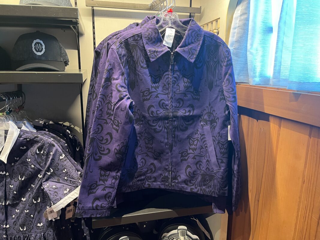 A purple jacket with a black, intricate pattern is displayed on a hanger in a retail store. Other similar apparel and accessories are visible in the background.
