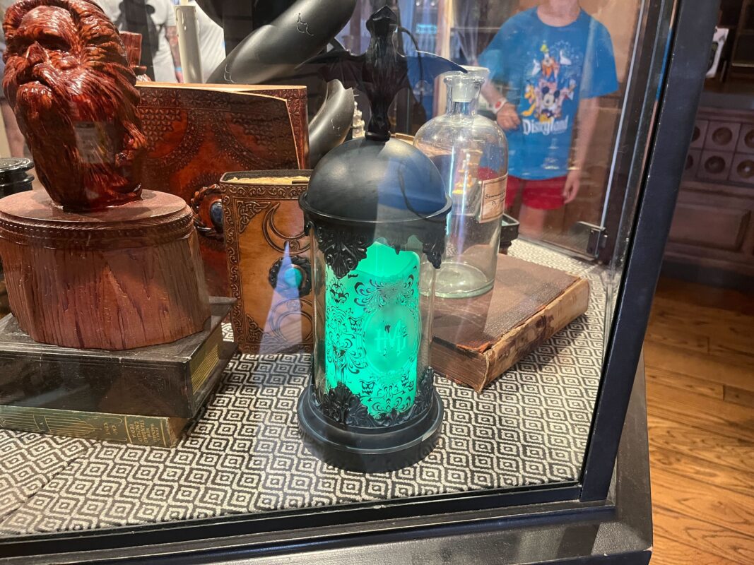 A display case featuring various decorative items including a glowing green lantern, a carved wooden figure, and some vintage bottles. A person is visible in the background outside the case.