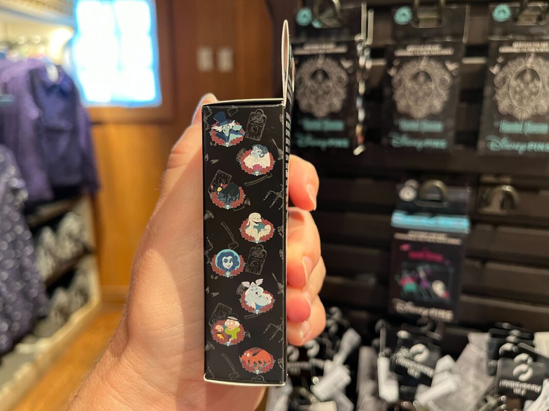 A hand holding a box featuring multiple circular character illustrations in a store with other similar boxes and items in the background.
