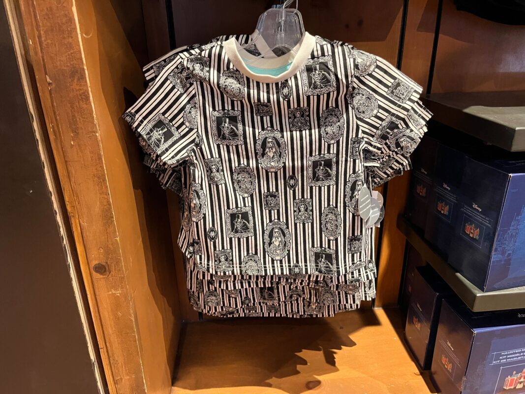A short-sleeve black and white striped shirt with various printed designs hangs on a wooden rack surrounded by blue boxed items.