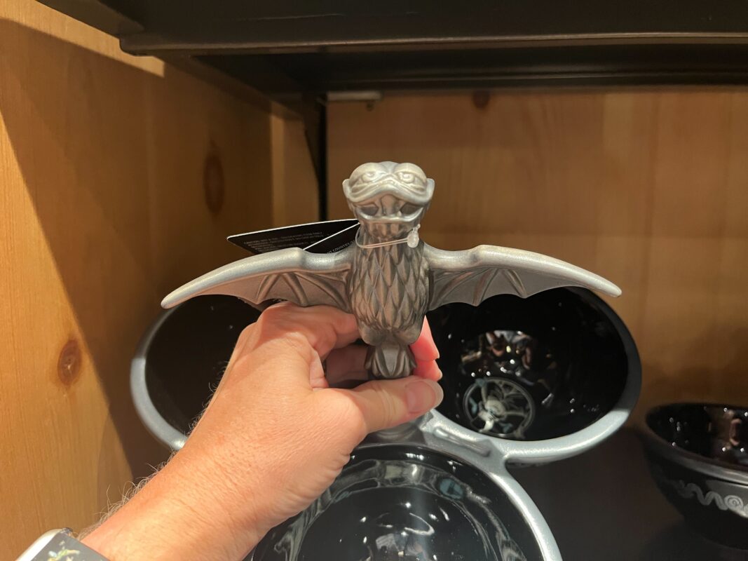 Person holding a silver dragon-shaped bottle opener in front of a wooden shelf displaying black bowls.