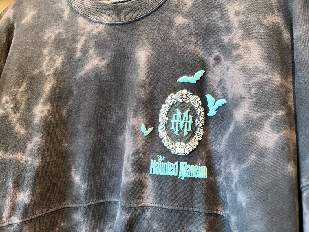 A sweatshirt featuring "The Haunted Mansion" logo with bats and decorative elements.