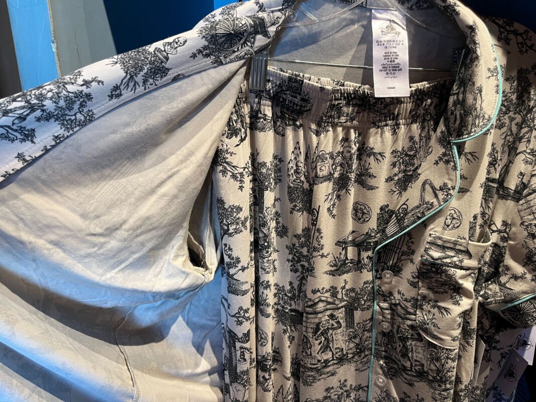 A pair of patterned pajamas on hangers, with designs of various scenes in black on white fabric, displayed in a store. The garments include a button-up shirt and matching pants.
