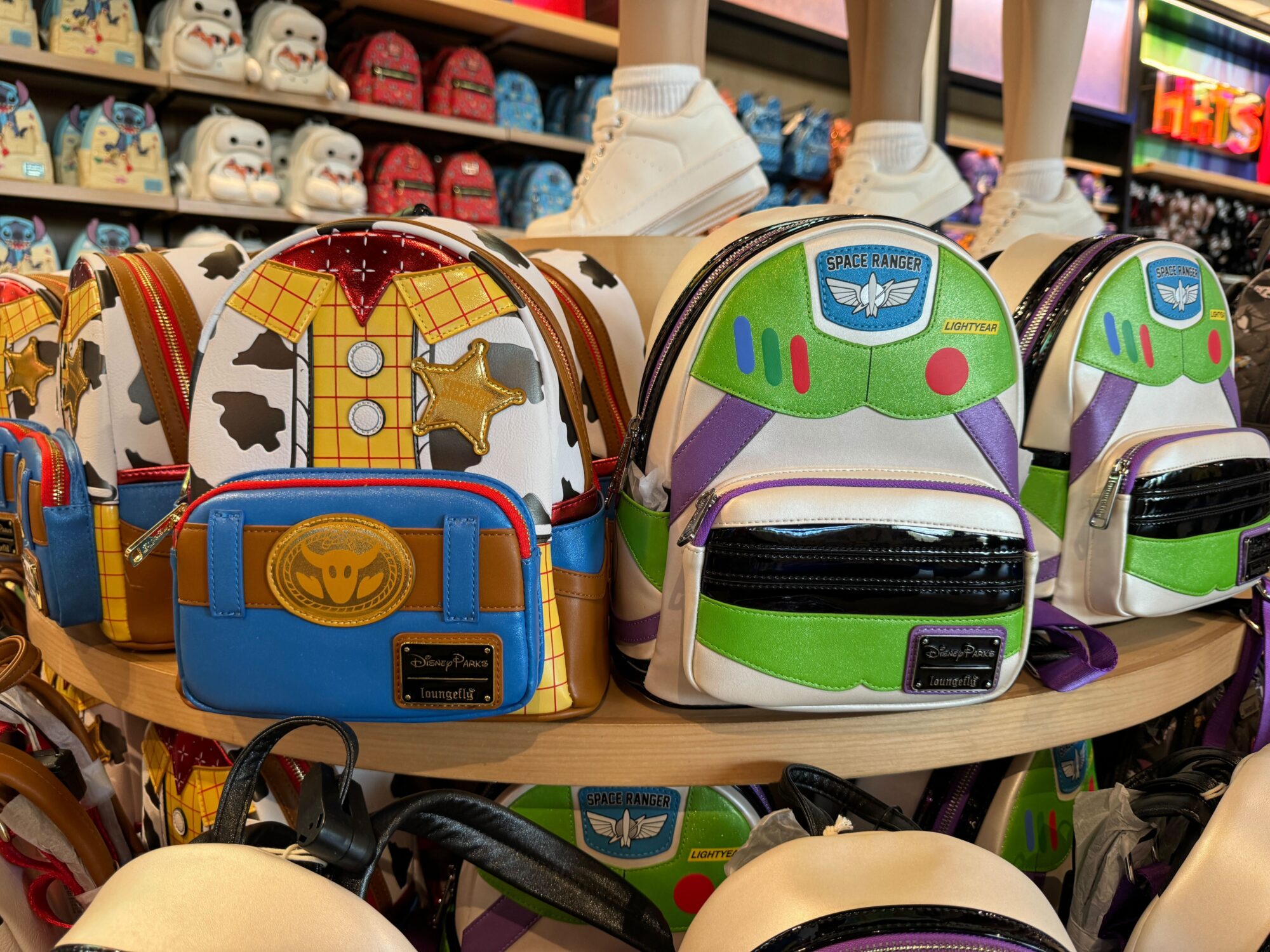 Display of colorful themed mini backpacks inspired by characters, arranged on a store shelf under mannequins wearing sneakers.