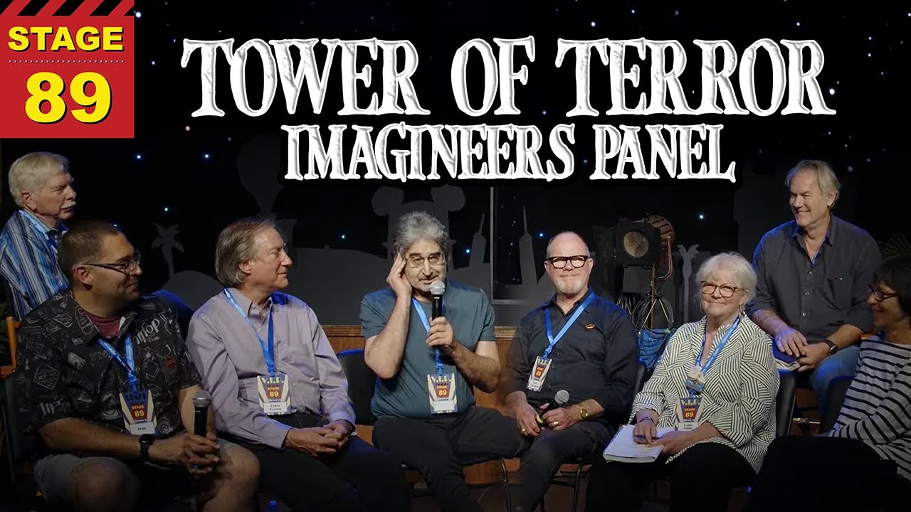 A group of eight people sits on a stage with a sign reading "30 Years of Twilight Zone Tower of Terror Imagineers Panel." Seven people are seated in chairs while one stands behind them.