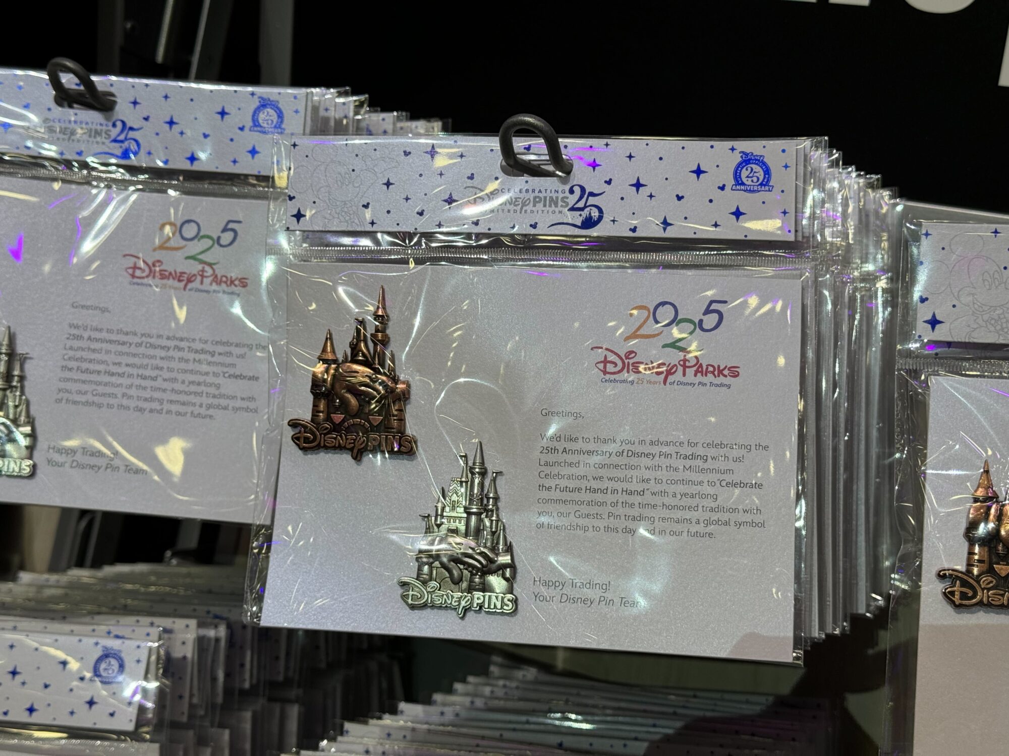 Display of Disney Parks 25th Anniversary Trading Pin Packs, featuring a letter and a castle pin in front of a starry background.