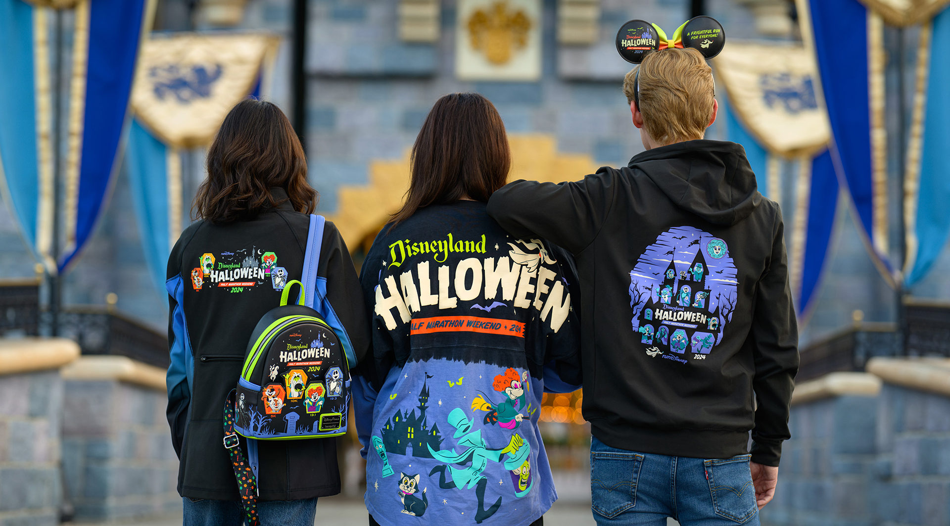 Three people are seen from behind wearing Disneyland Halloween-themed clothing and accessories while standing in front of a castle.