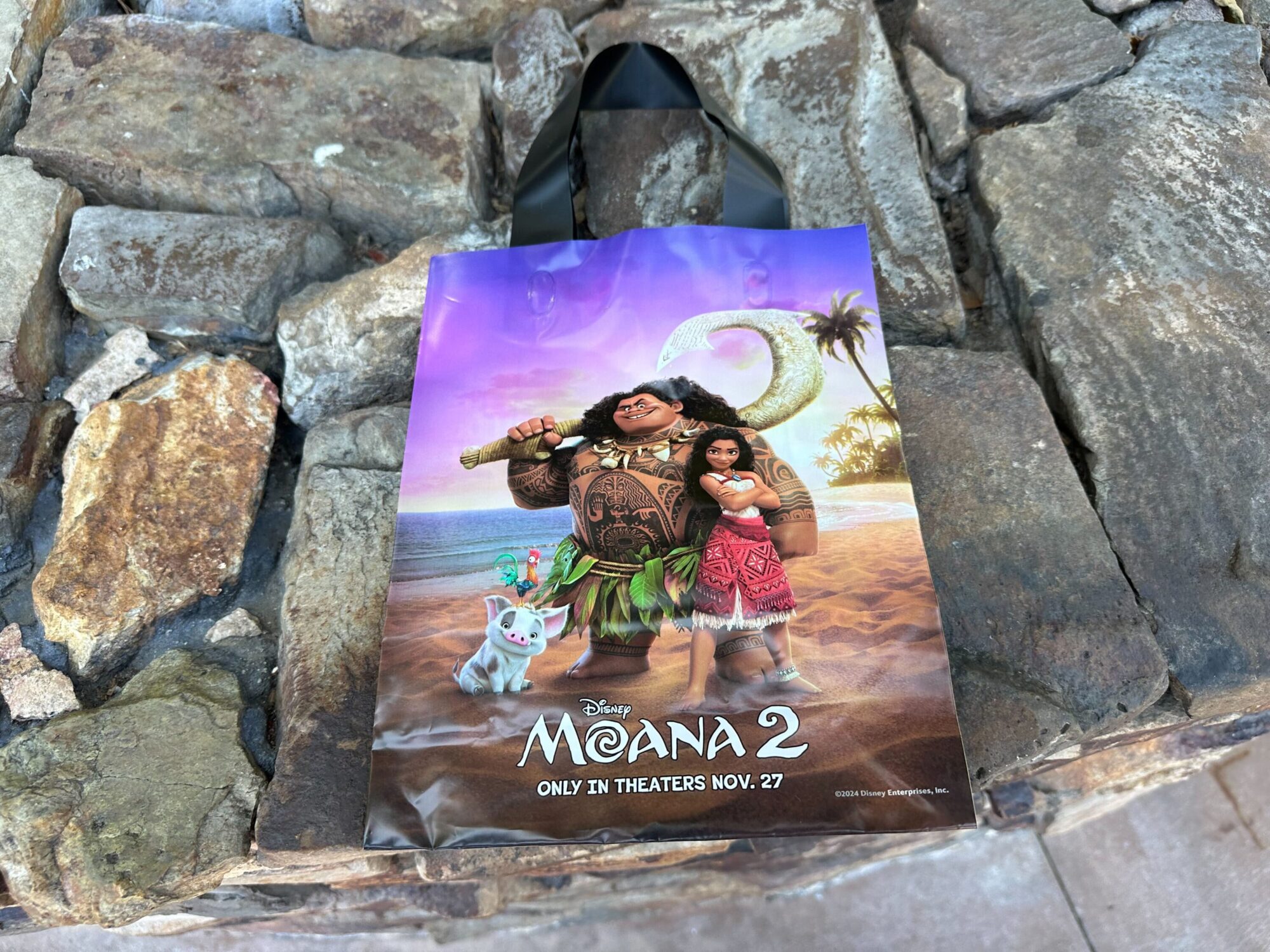 A shopping bag featuring characters from "Moana 2" against a rocky background. It advertises the movie's release date as November 27.