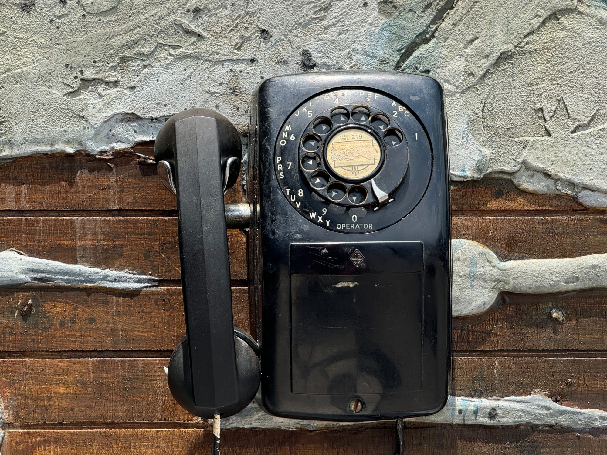 A vintage rotary dial telephone with a black handset is mounted on a textured wooden surface with peeling paint, reminiscent of an eerie scene straight out of Halloween Horror Nights.