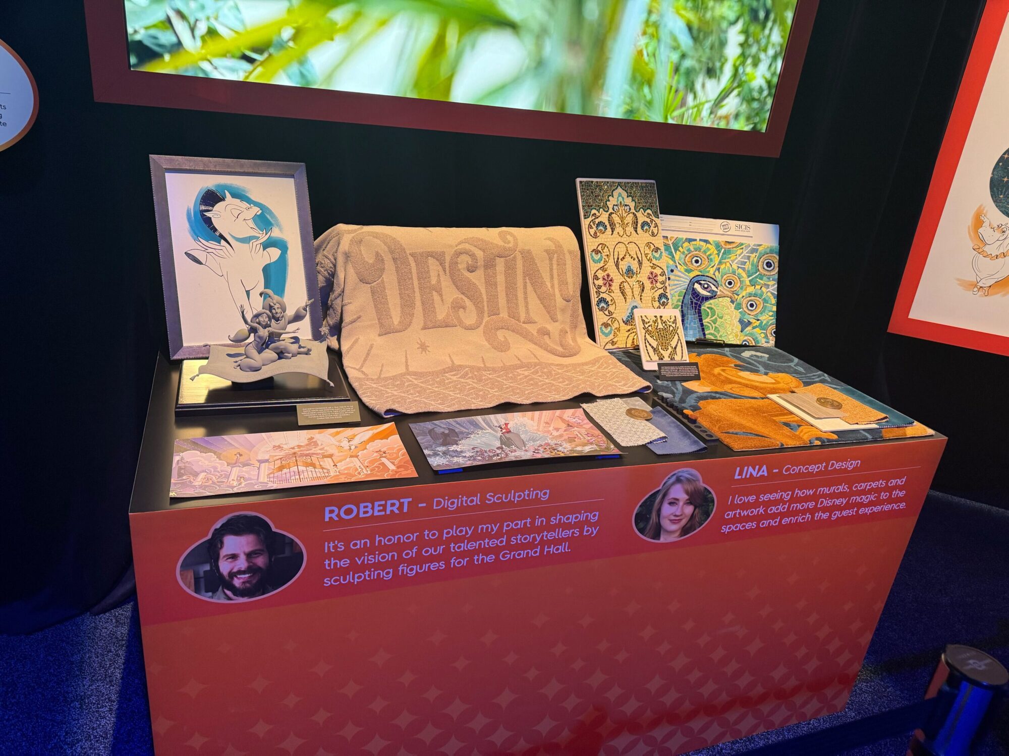 A display table showcases various art pieces, including sketches, digital illustrations, and a textured cloth with "DESIGN" printed on it. Two artist profiles, Robert and Lina, are highlighted.