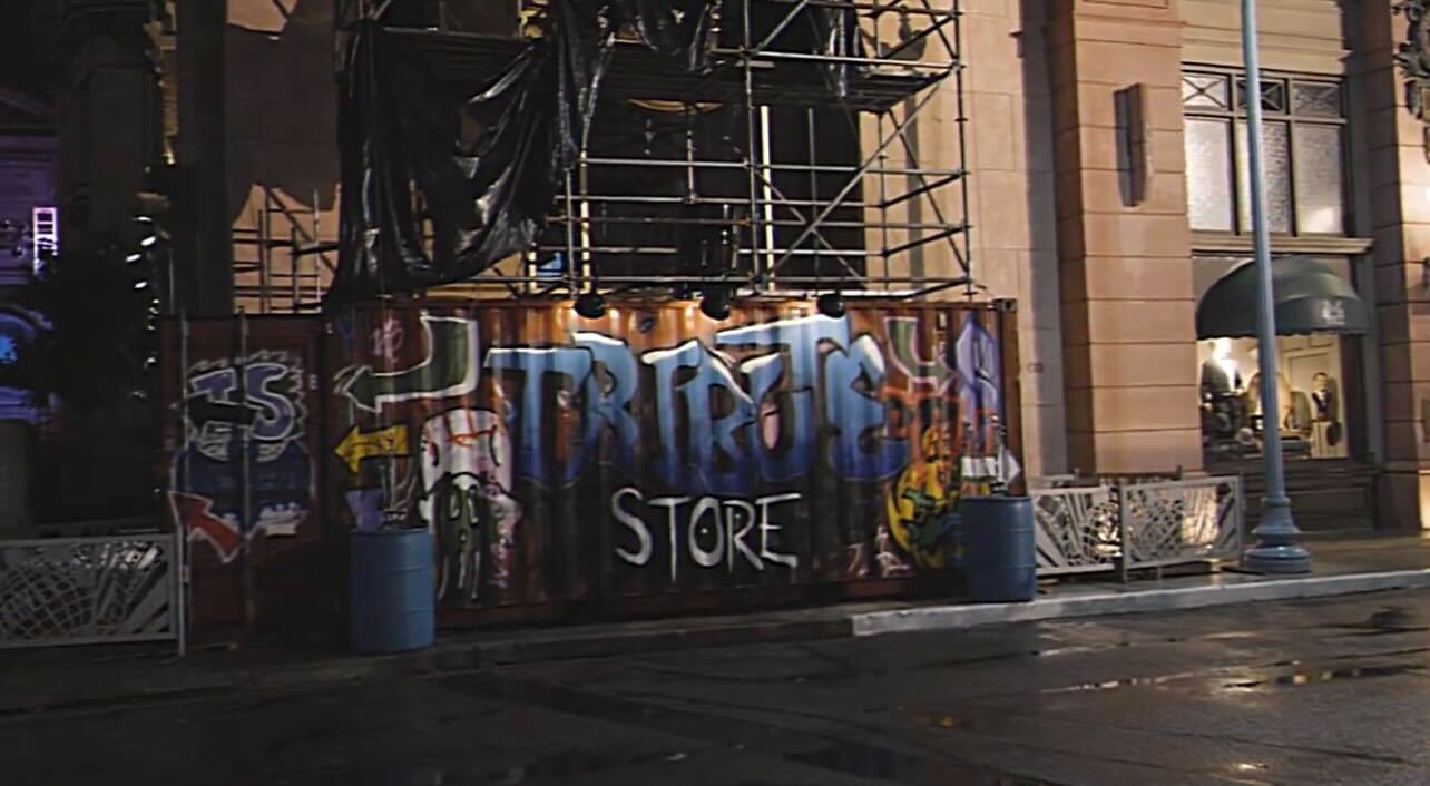 Graffiti-covered wooden boards with the words "TRASH STORE" under a scaffold in front of a building at night.
