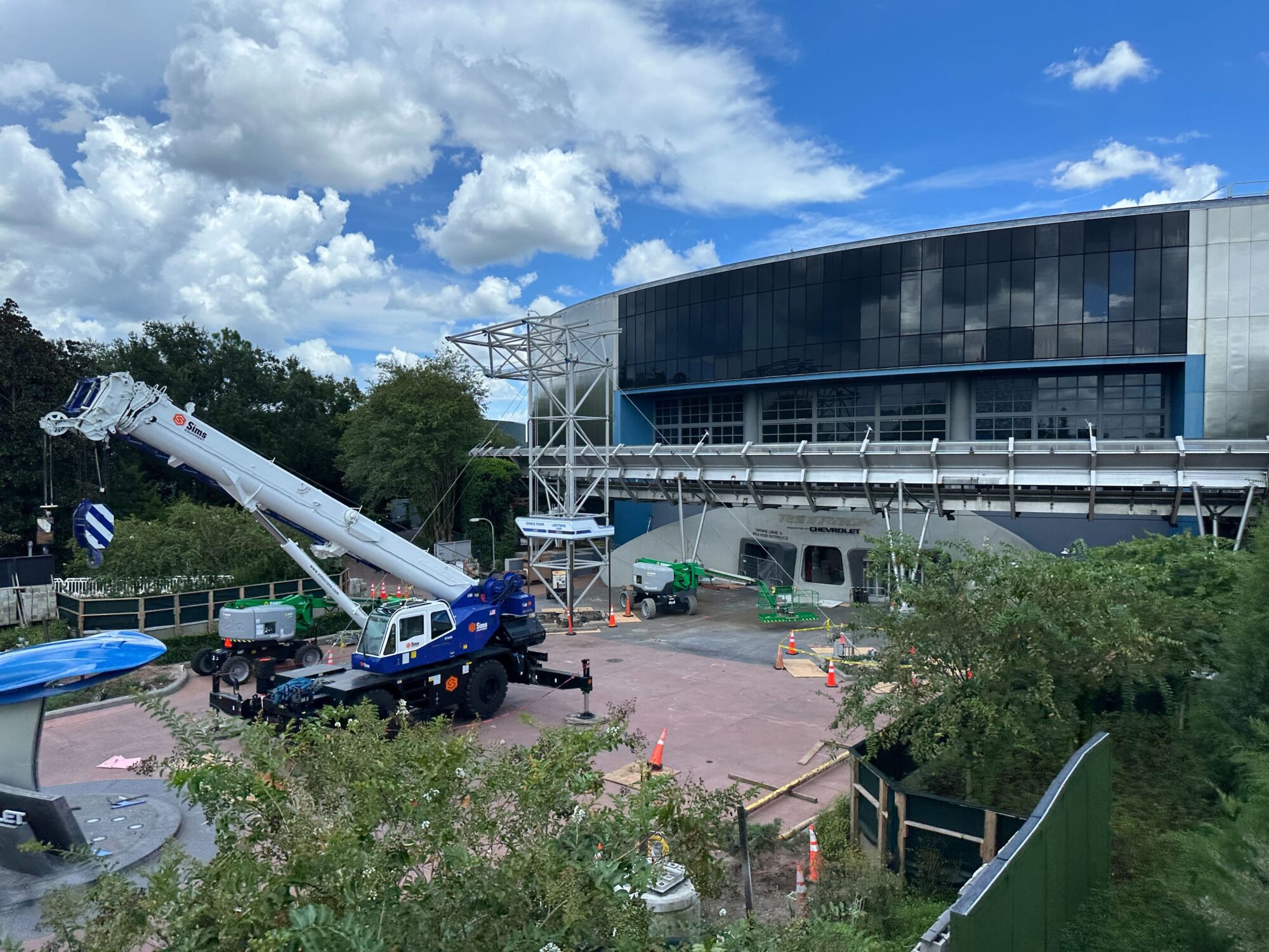 A construction site featuring a crane and construction equipment in front of a modern, curved building under a partly cloudy sky.