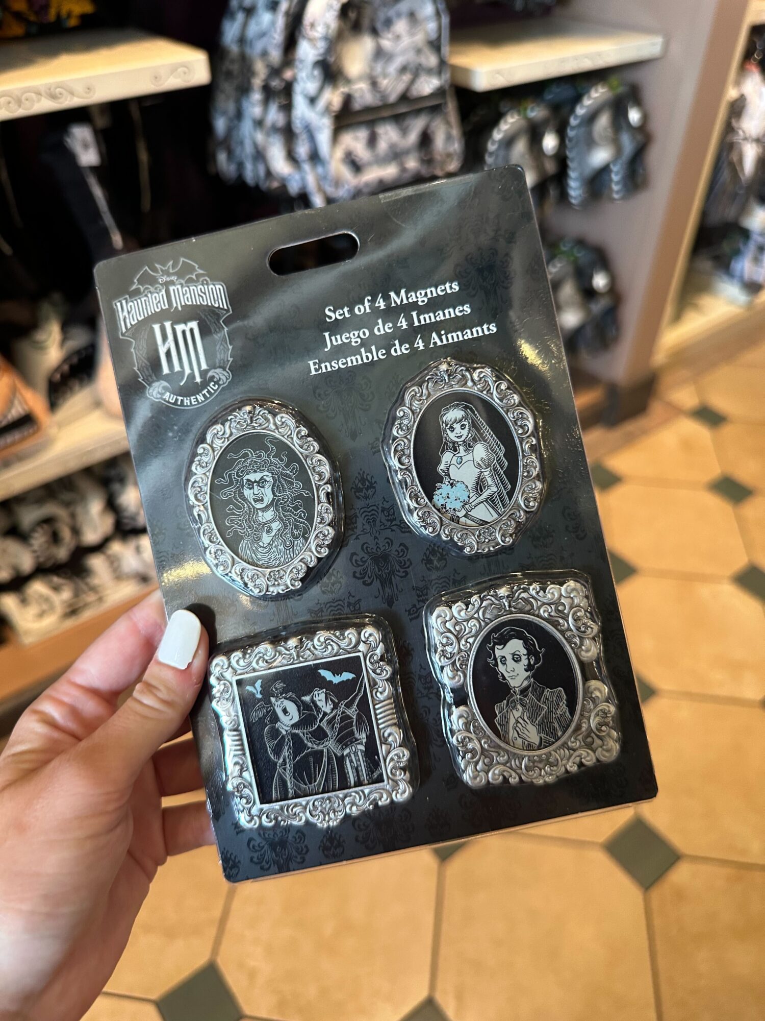 A person holds a carded set of four Haunted Mansion-themed magnets in a store at Walt Disney World. The magnets, part of the new Halloween 2024 merchandise, feature vintage-style designs of characters from the ride.