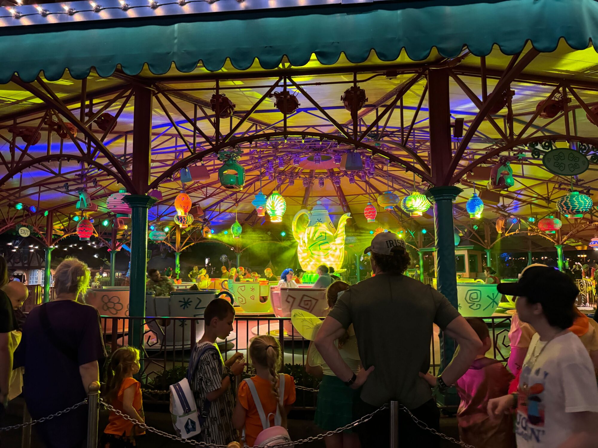 A brightly lit carousel with colorful lanterns and decorations stands out at Mickey’s Not-So-Scary Halloween Party 2024. People, including children, are standing around and inside it, observing the ride at Magic Kingdom.