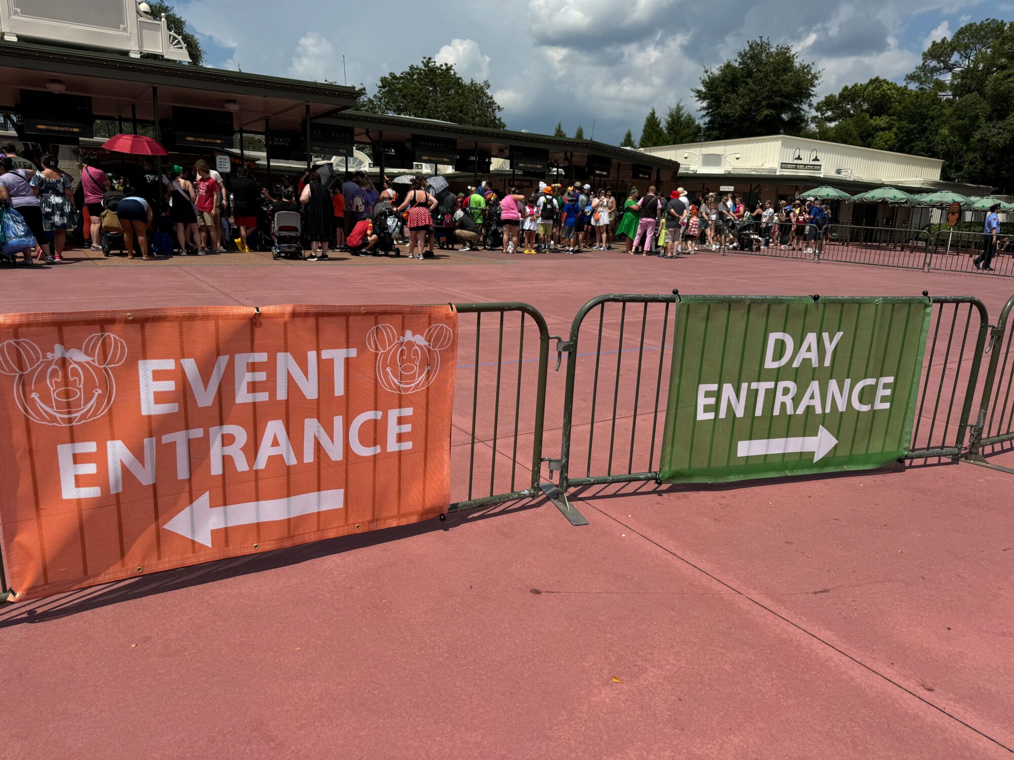 People lining up at the event and day entrances, separated by fences with signs indicating "Event Entrance" to the left and "Day Entrance" to the right.