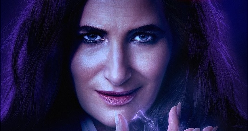 Close-up of a person with long dark hair and intense eyes, holding illuminated purple energy between their fingers against a dark background, reminiscent of the mysterious aura in "Agatha All Along.